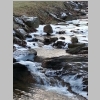 This is a photograph of a rocky, swift flowing river, with ice frozen on its rocks.